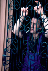 Man smoking stands in doorway behind a metal fence