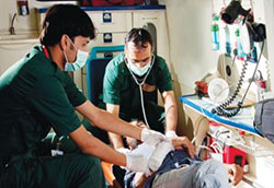Two medical workers in an organized ambulance work with an injured patient reclined on a mobile stretcher.