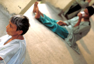 A man up close seated on the floor stares off camera; one in the background, out of focus, also seated on the floor