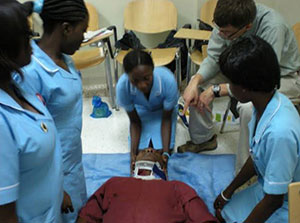 Woman in medical uniform braces neck of man with neck brace lying on table, another man stands close and instructs, 3 observe