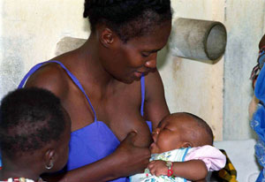 Woman breastfeeding a young baby, a young child seated next to the mother looks on