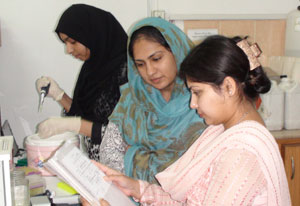 Dr. Sadaf Naz works in lab with two other women researchers, observing notes