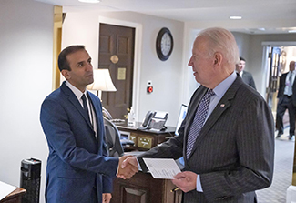 The photo shows Dr. Raj Panjabi shaking President Biden’s hand in the West Wing of the White House. Both men wear dark suits and the figures of security officers can be seen in the background.