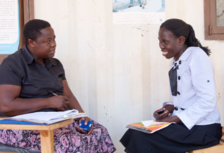 Female researcher collects data with pen and paper from female research participant who is seated across from her