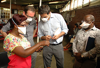 Researchers wearing surgical masks collaborate around a mobile device
