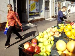 Crates of fruit at street market, woman walks by in background, man browses market