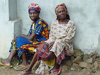 Two older women in Nigeria seated outdoors on a pile of rocks