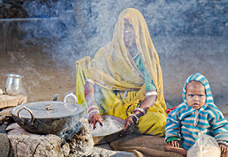 Woman seated next to smoking stone cookstove, young child seated next to her