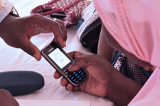 Woman wearing scarf on head views cell phone screen and presses keys, another hand steadies the device for her