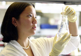 Female researcher in lab holds up and observes contents of a flask