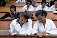Female students in white lab coats seated in lecture hall take notes