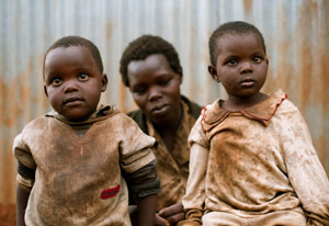 Two young children in very dirty clothes, parent seated in background looking down