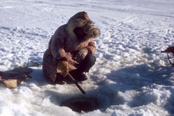 Photo: Surrounded by snow, a person in a thick, fur-lined winter coat fishes in the ice