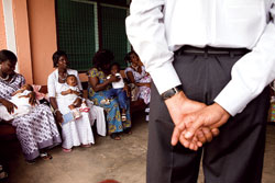 President Obama, seen from the back, stands in front of African women with infants and children on their laps