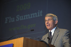 NIAID Director Dr. Anthony Fauci speaks at a podium, on screen in background a slide reads 2009 Flu Summit www.flu.gov