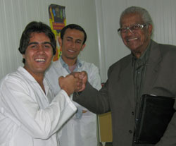 Iranian male doctor in lab coat shares a fist bump with Dr. Aaron Shirley, another Iranian male doctor observes