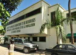 Photo: Outside of a tan building with a sign in green text on the side, text is too small to read, the first GIESKO clinic