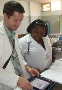 Photo: male and female researchers, both standing in lab wearing white lab coats, view iPad placed on desk