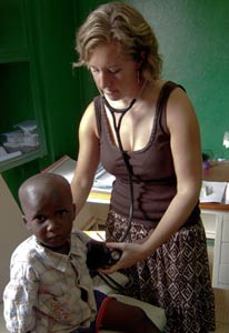 Dr Manning in an exam room with stethoscope in ears holds it to a young boy’s back, she looks down at him