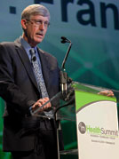 Dr Francis S Collins speaks into microphone at podium, sign reads mHealth Summit on front of podium