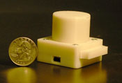 Small, white lens-free microscope, pictured alongside a quarter, which is about half the height of the microscope