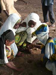 Photo: Four young Nigerian girls with scarves on their heads squat, and play and dig in the dirt with their hands