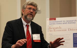 Photo: Dr. Sten Vermund, speaking, motions with his hands, in front of poster filled with small text