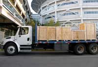 Large truck parked at side of road, large buildings in background, four large crates strapped to the bed