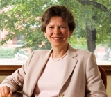 Dr. Karen Antman sitting at a desk with a tree outside in the background. Photo: BU Photo Services.