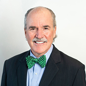 Headshot of Dr. Peter Kilmarx who is smiling and wearing a dark blue jacket, a light blue shirt, and a green bow tie with white polka dots