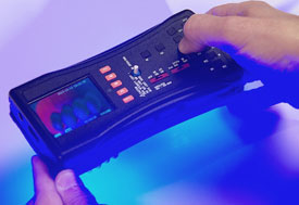 Close up of hands holding FDA Counterfeit Detection Device-3 CD-3, black electronic box with many buttons emits glow on bottom