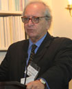 PHOTO: Dr. Eduardo E. Castilla speaks into a microphone at a podium, with shelves of books behind him.